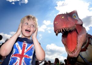 Young boy holding ears next to large dinosaur