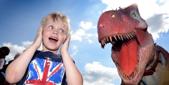 Young boy holding ears next to large dinosaur